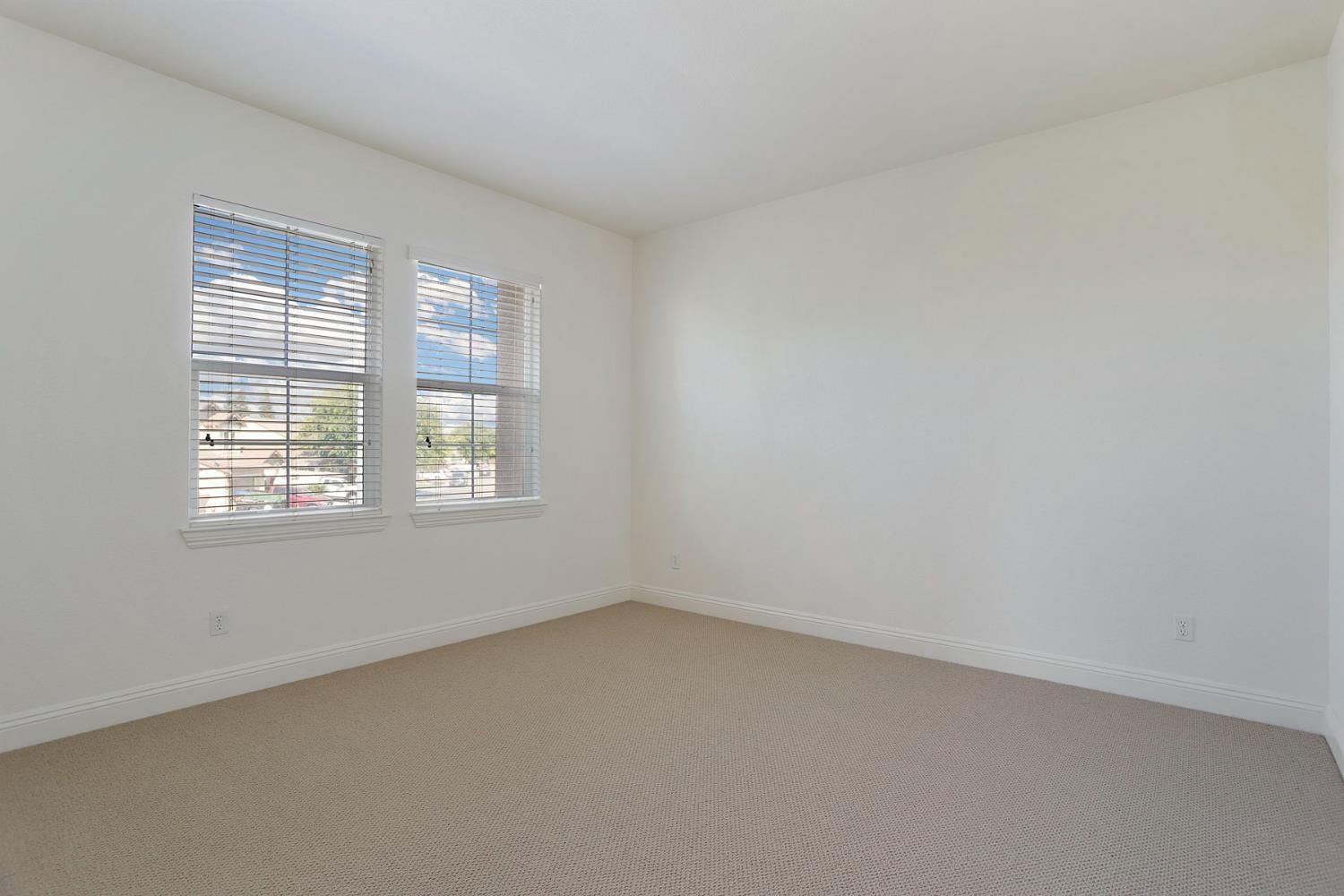 Empty carpeted room with two windows and white blinds.