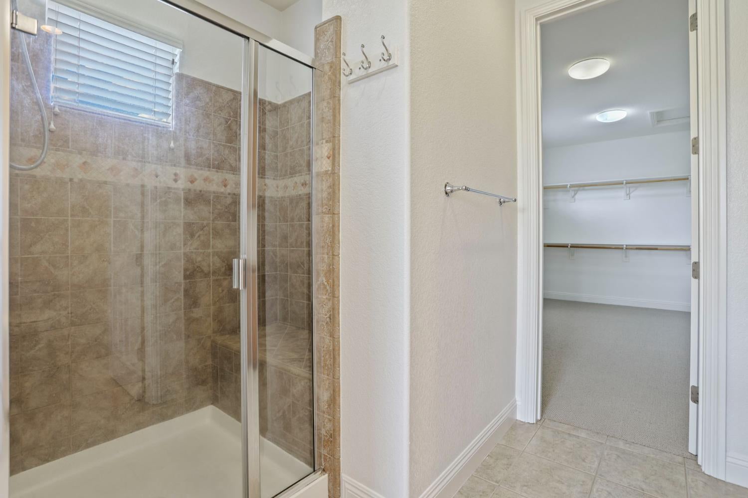 Bathroom with a beige-tiled glass shower beside an open, empty walk-in closet.
