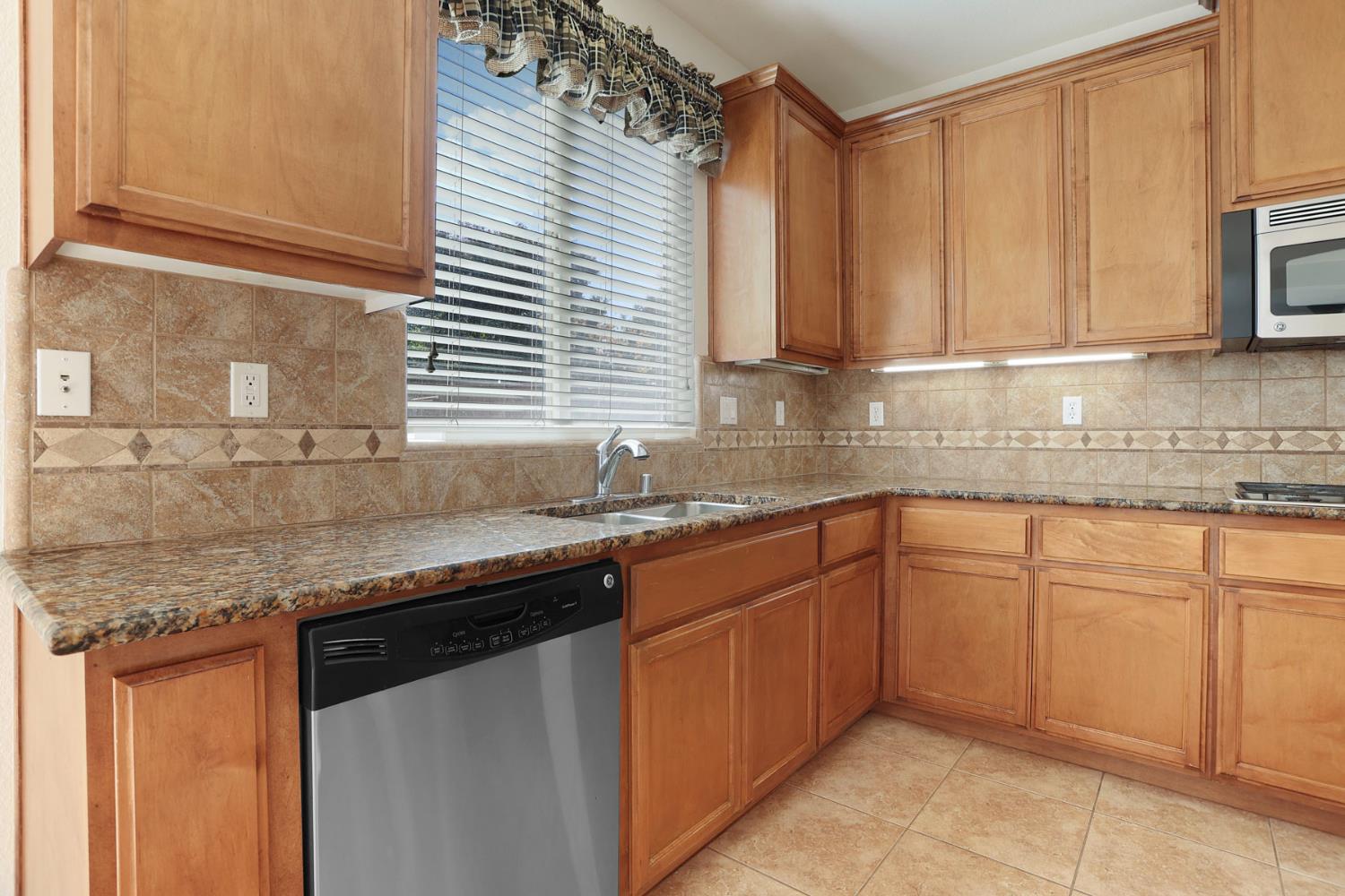 Kitchen with wood cabinets, granite counters, patterned tile backsplash, and a window above the sink.