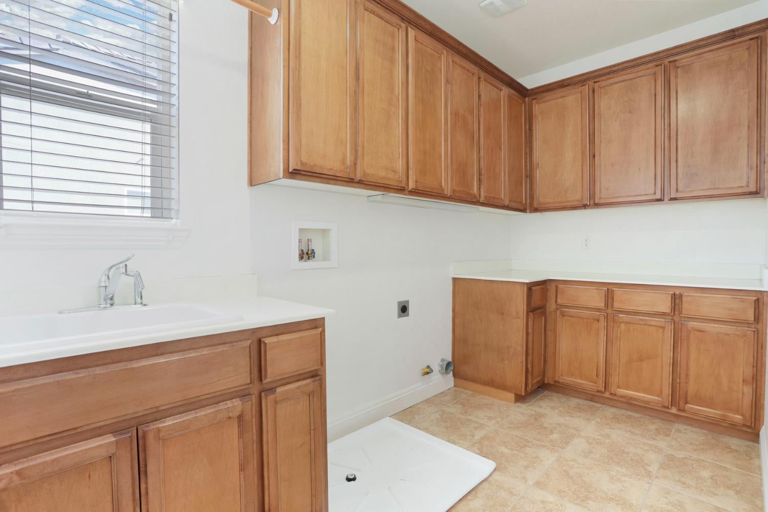 Laundry room with wood cabinets, a white utility sink, and washer drain pan on the floor.