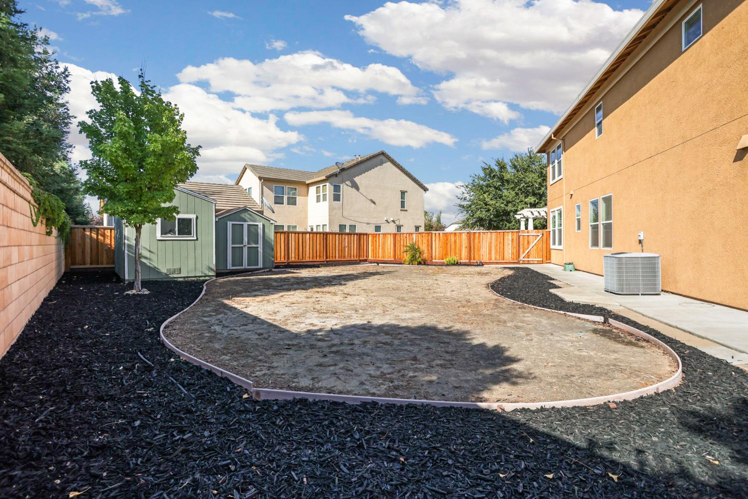 Fenced backyard with a green storage shed, curved yard borders, and a large bare central area.