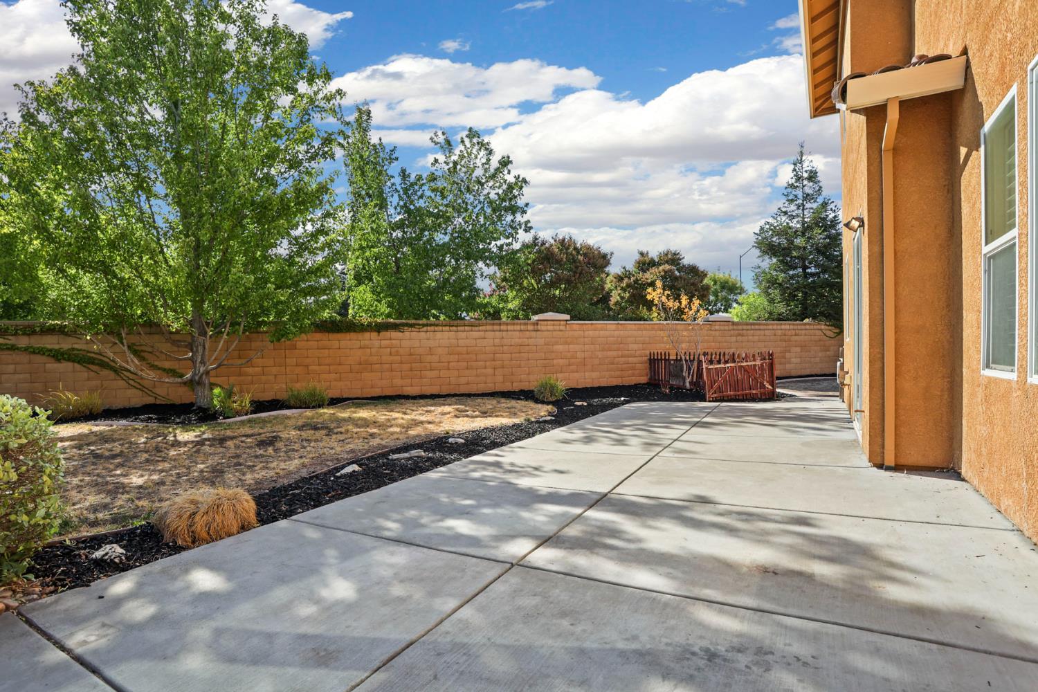 Backyard patio beside the stucco house, with a block wall and landscaped yard.
