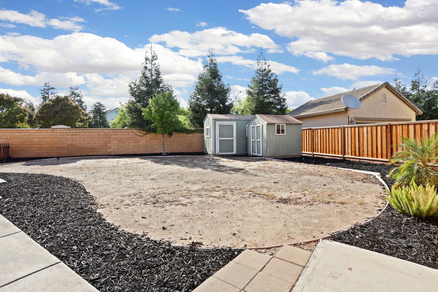 Backyard with a broad bare garden area, two storage sheds, and block and wood fencing.