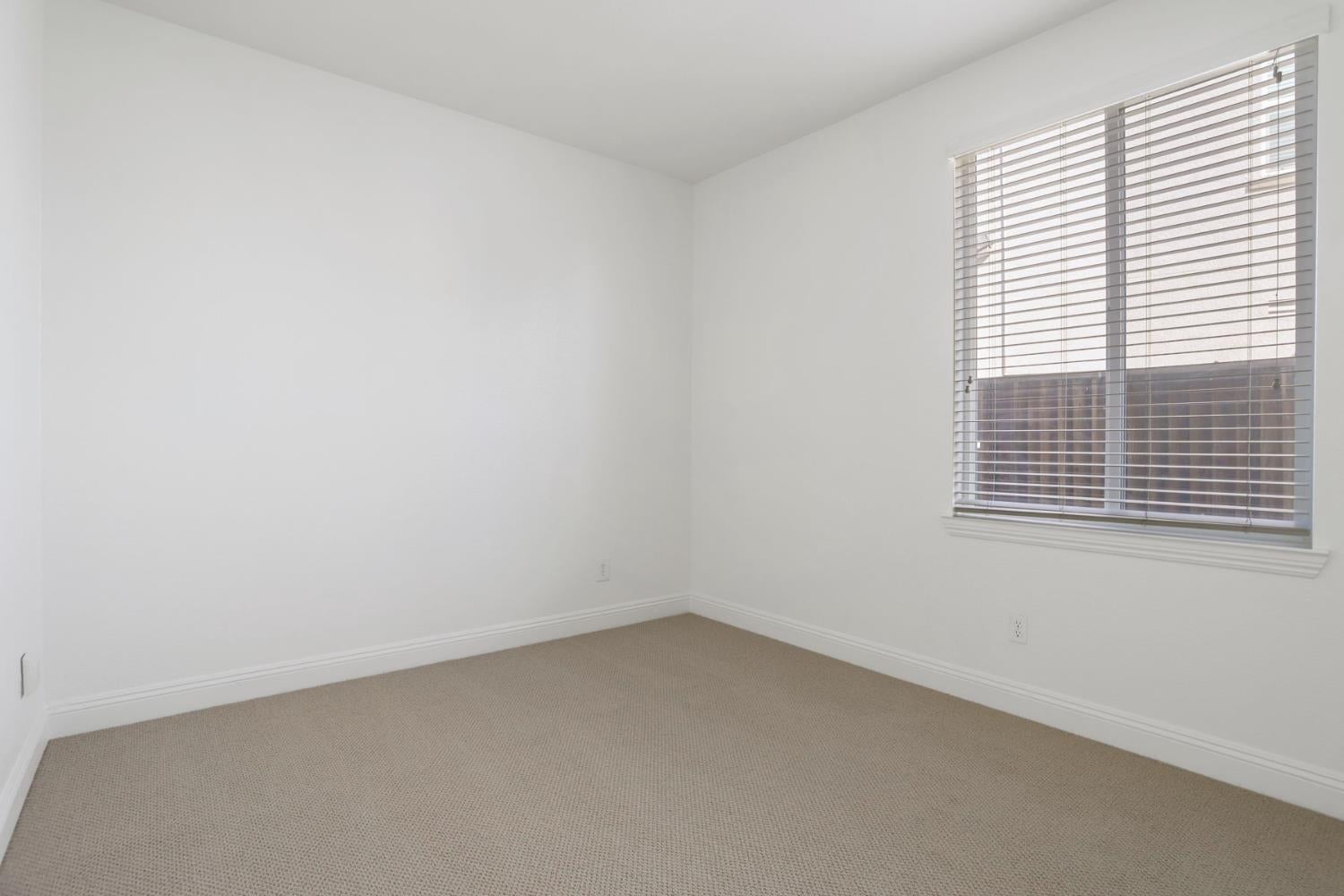 Empty carpeted room with white walls and a large window with blinds.