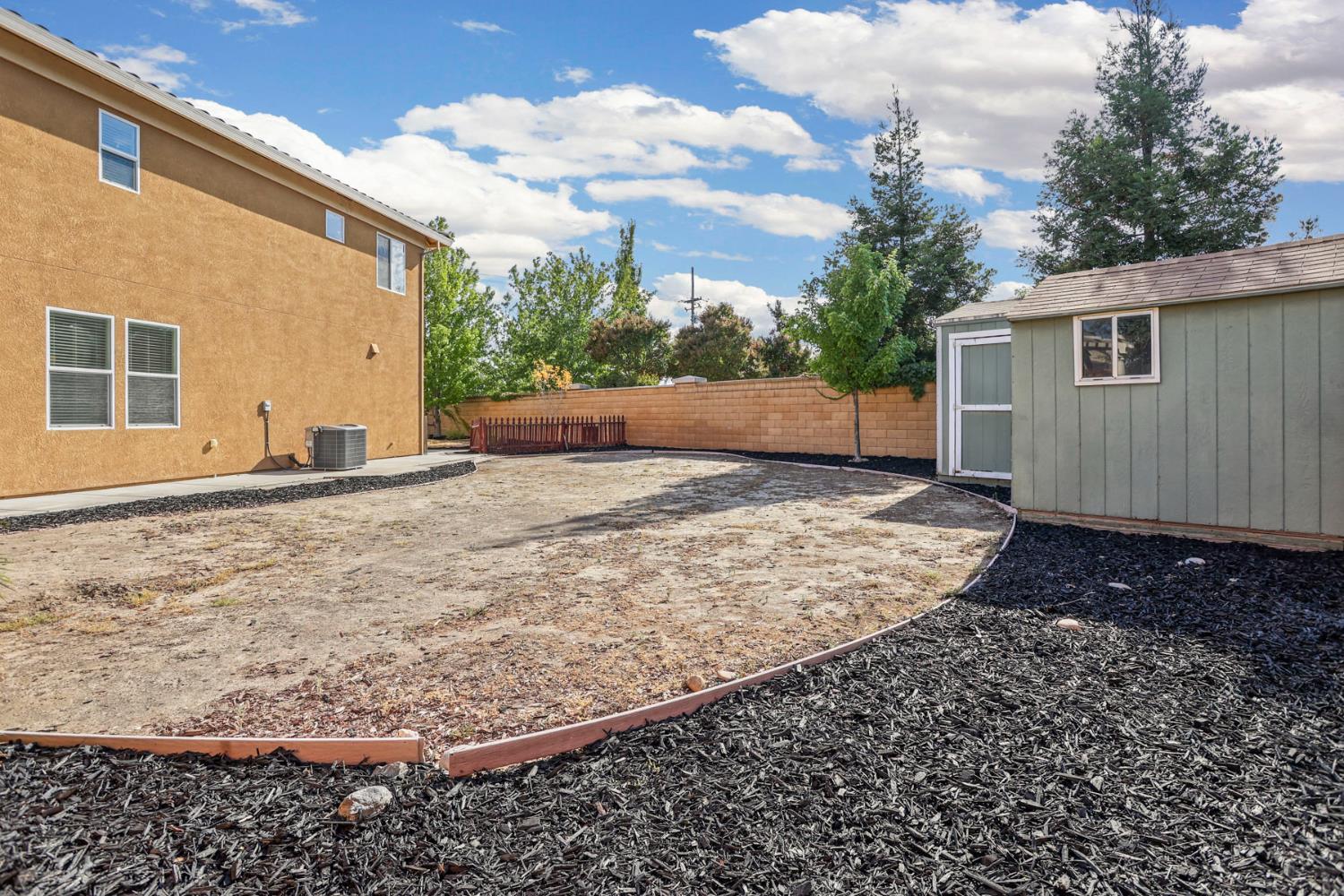 Backyard with a mostly bare dirt area, dark mulch borders, and a green storage shed.