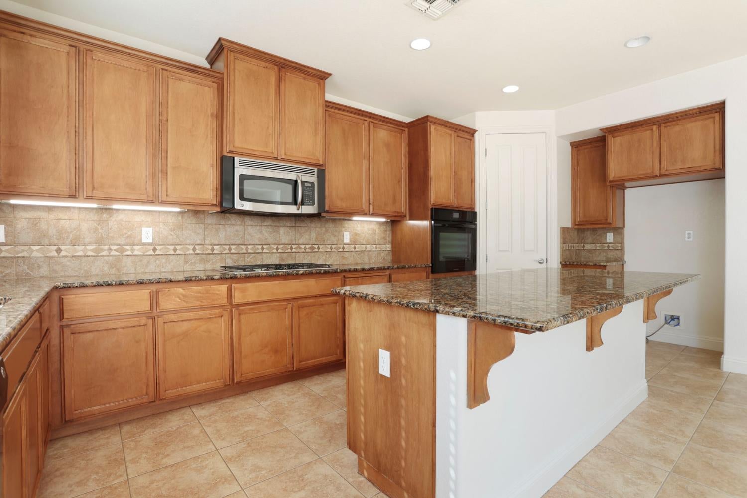 Kitchen with extensive wood cabinetry, tiled backsplash, and a granite-topped peninsula.
