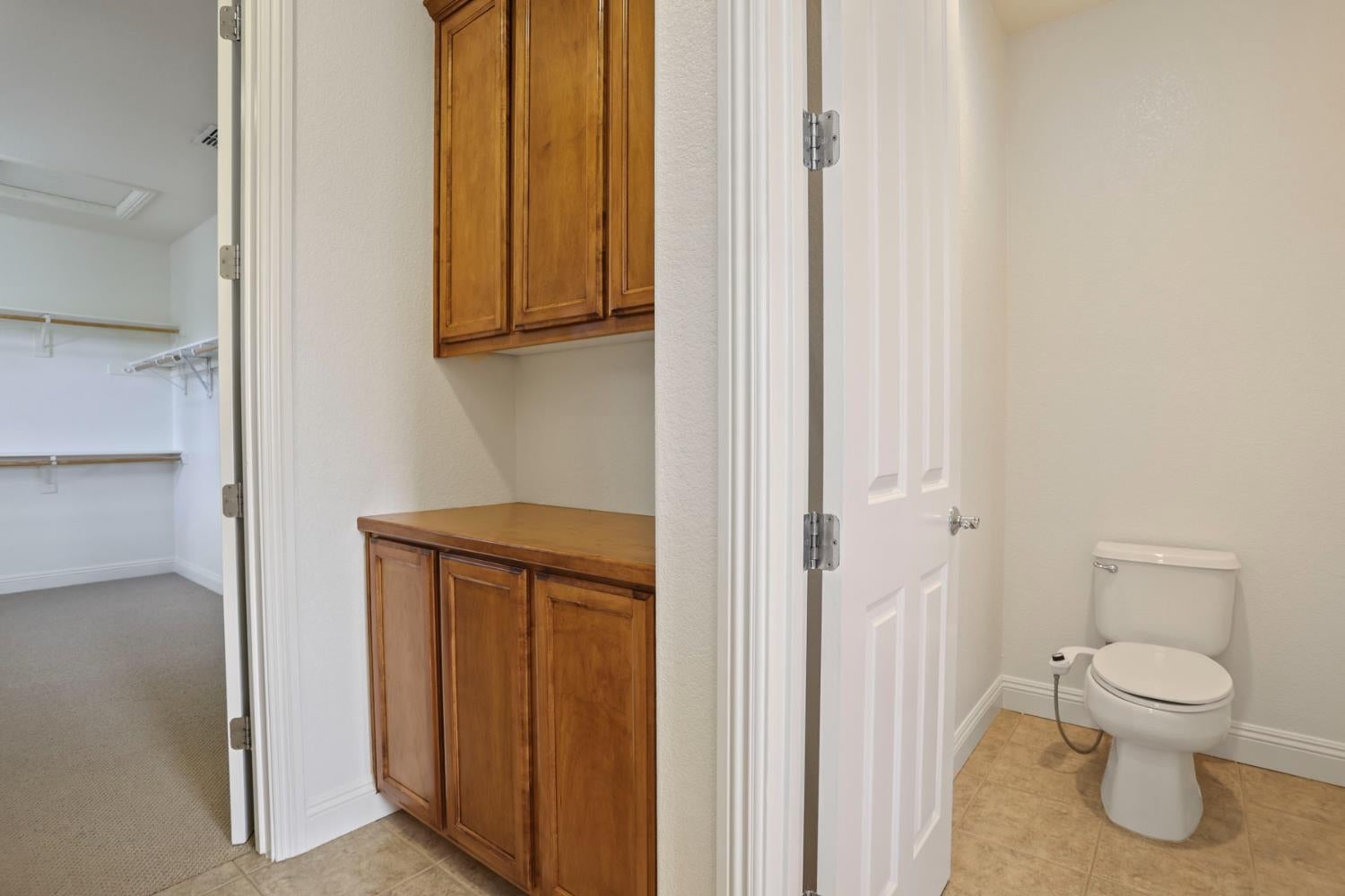 Bathroom with a toilet and tile floor beside a wooden built-in vanity and walk-in closet.