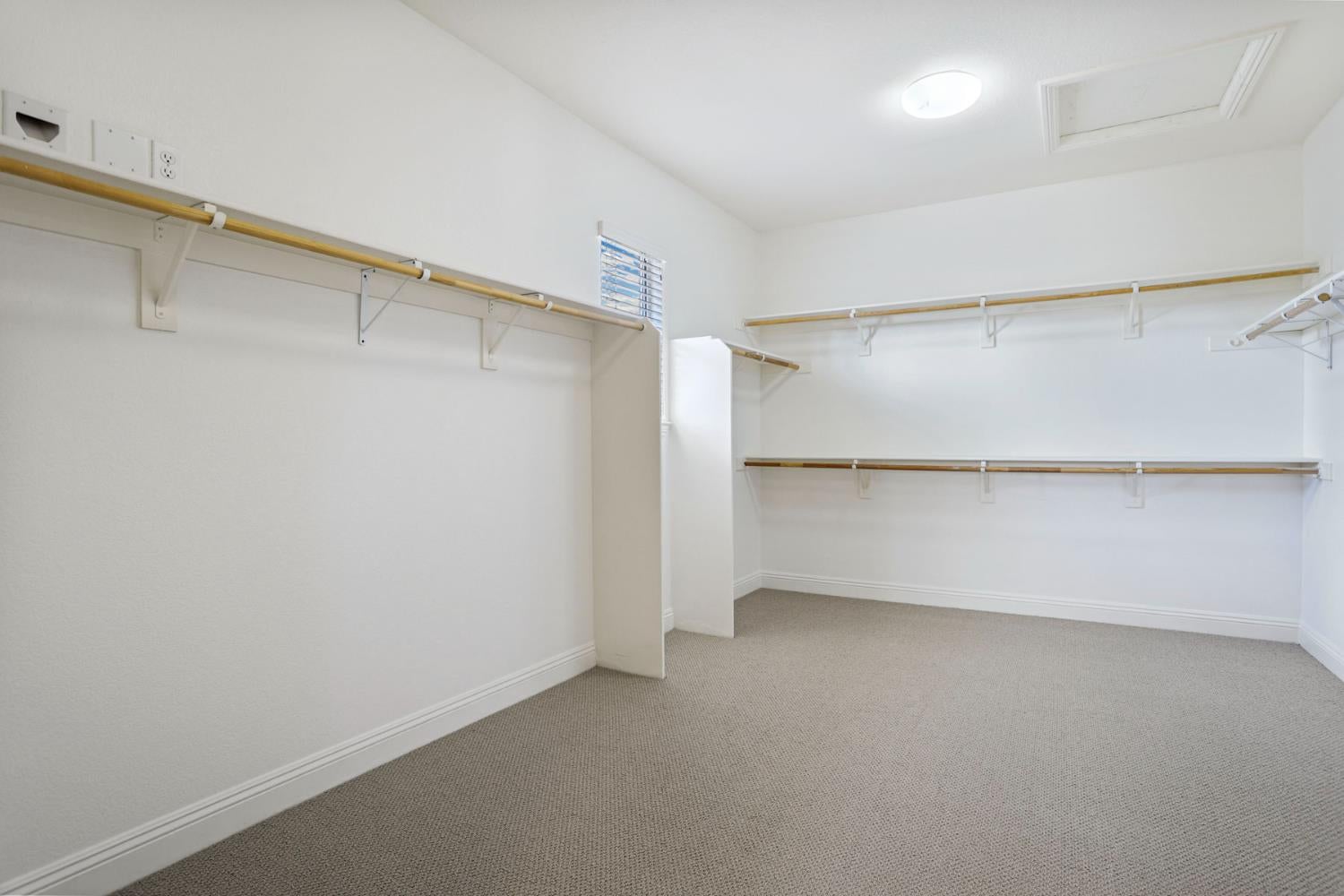 Empty walk-in closet with wraparound wooden hanging rods, shelves, and beige carpet.