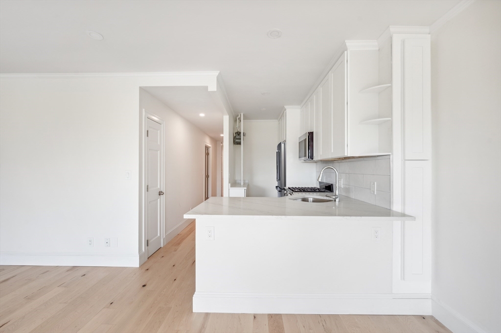 Unfurnished apartment kitchen with white cabinets, a peninsula countertop, and light wood floors.