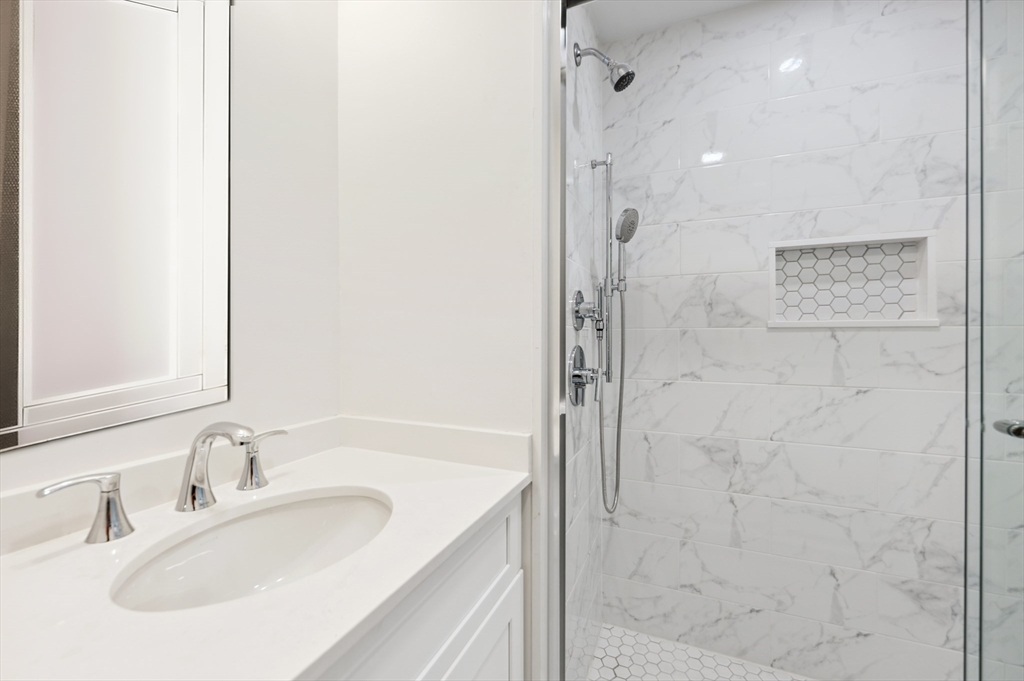 Bathroom with a white vanity and marble-look shower featuring a hexagonal-tile niche.