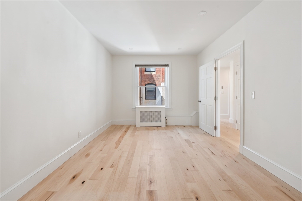 Empty room with pale hardwood floors, a window, and an open doorway.