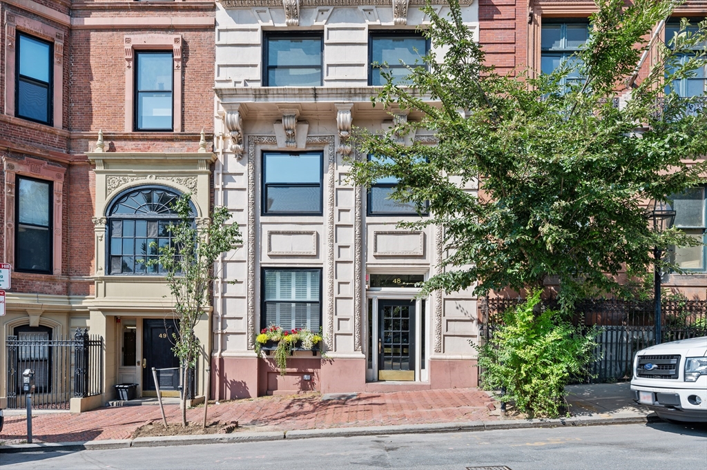 Ornate stone-and-brick building at 48 Beacon St, with a recessed glass entrance and leafy street tree.