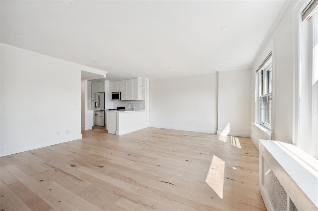 Vacant living area with pale wood floors, large windows, and an open kitchen.
