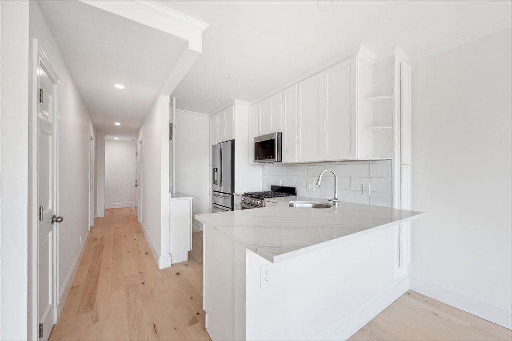 Kitchen with white cabinets, stainless steel appliances, a large island, and pale wood floors.