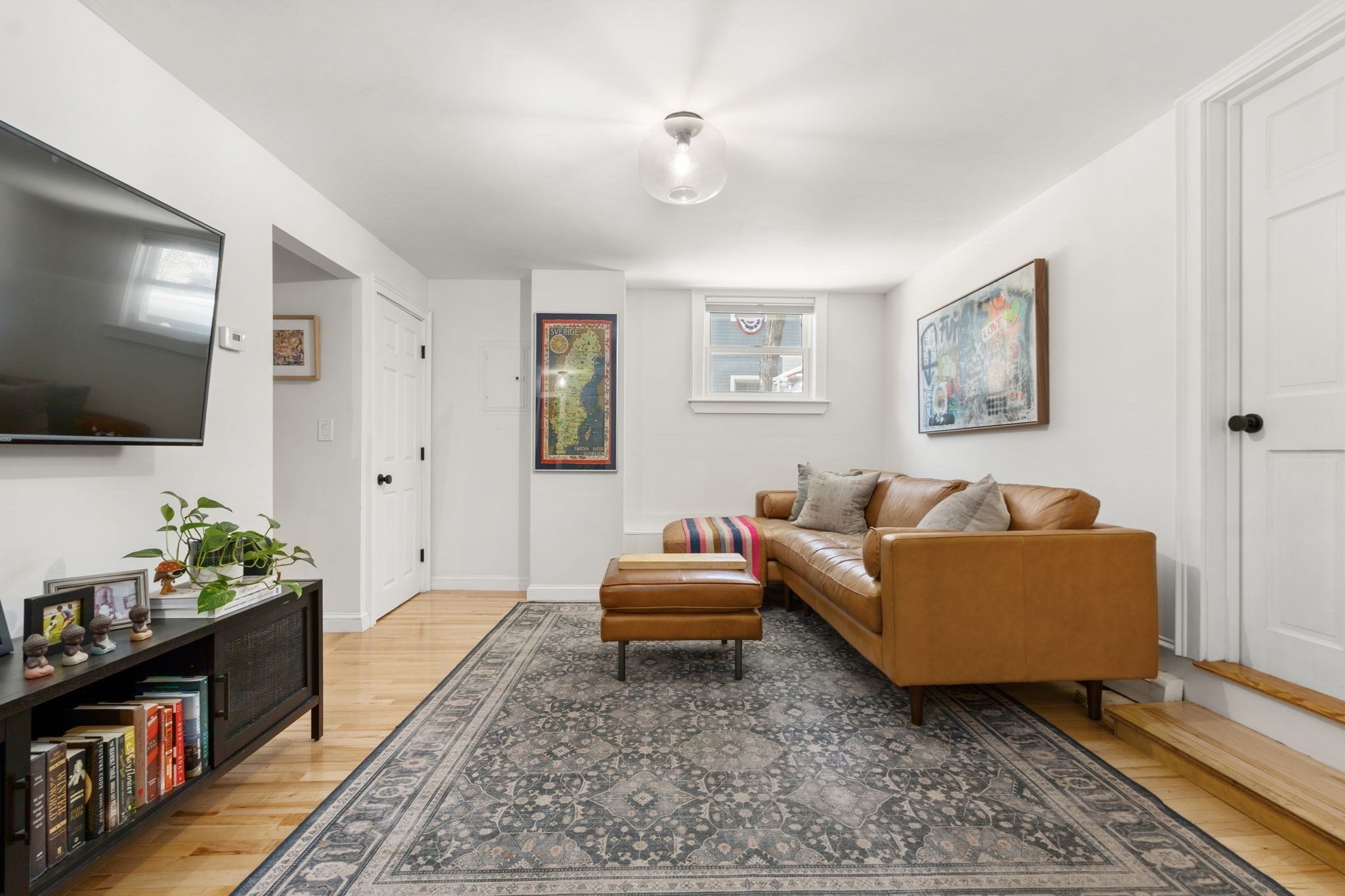 Furnished living room with a tan leather sectional, patterned rug, and wall-mounted television.
