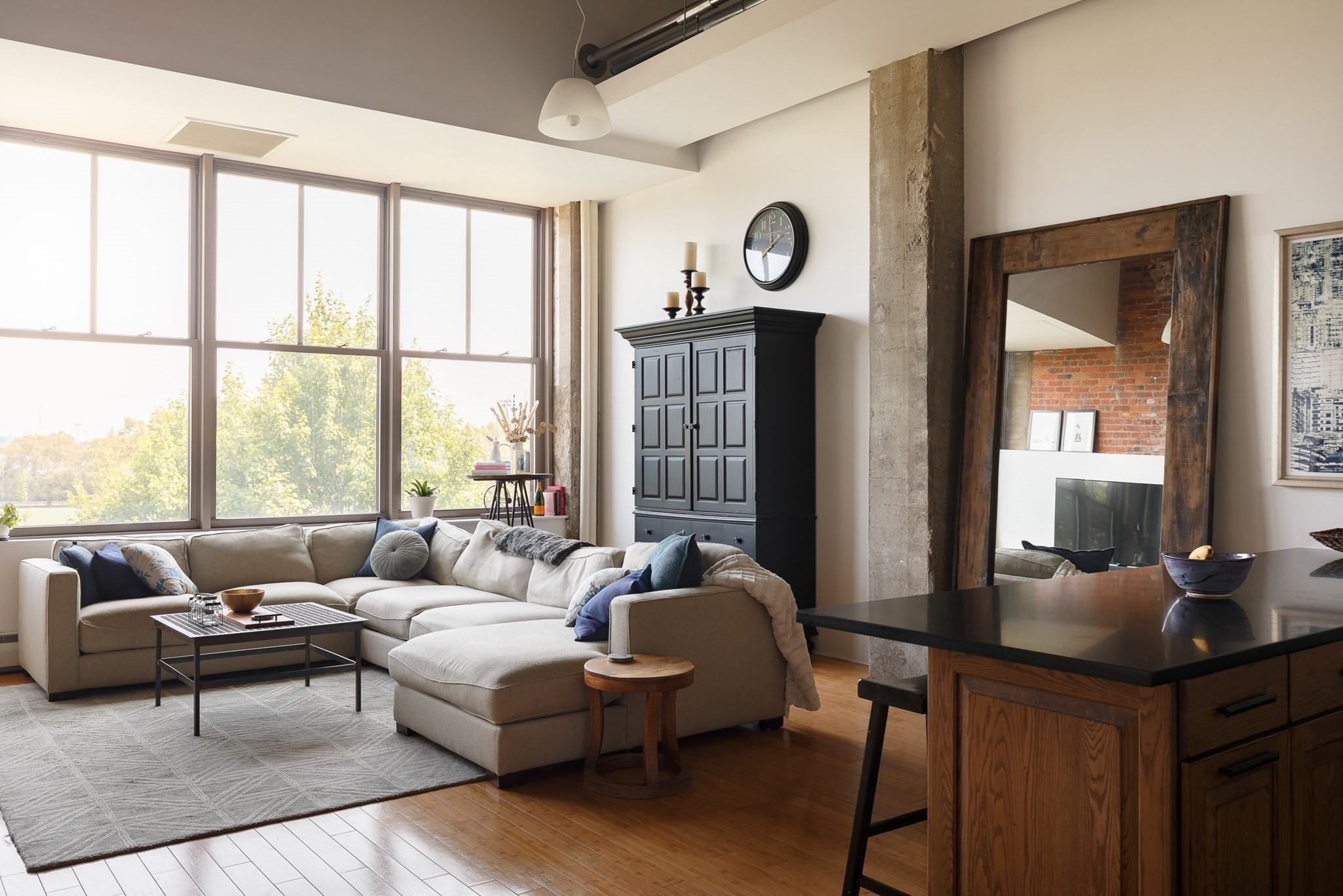 Furnished living room with a large sectional, tall windows, exposed concrete columns, and hardwood floors.