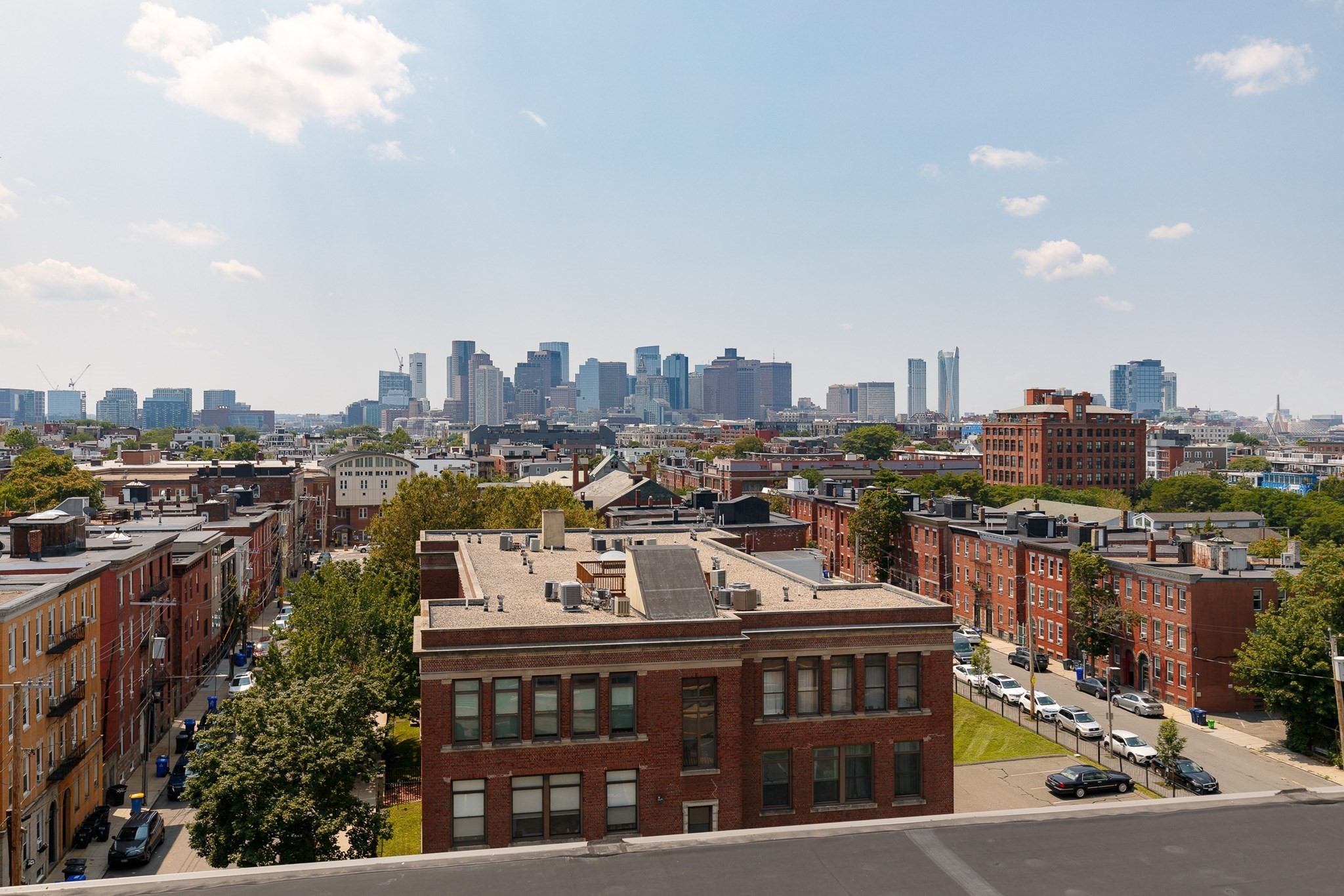 Boston skyline beyond red-brick buildings and tree-lined streets, viewed from above.