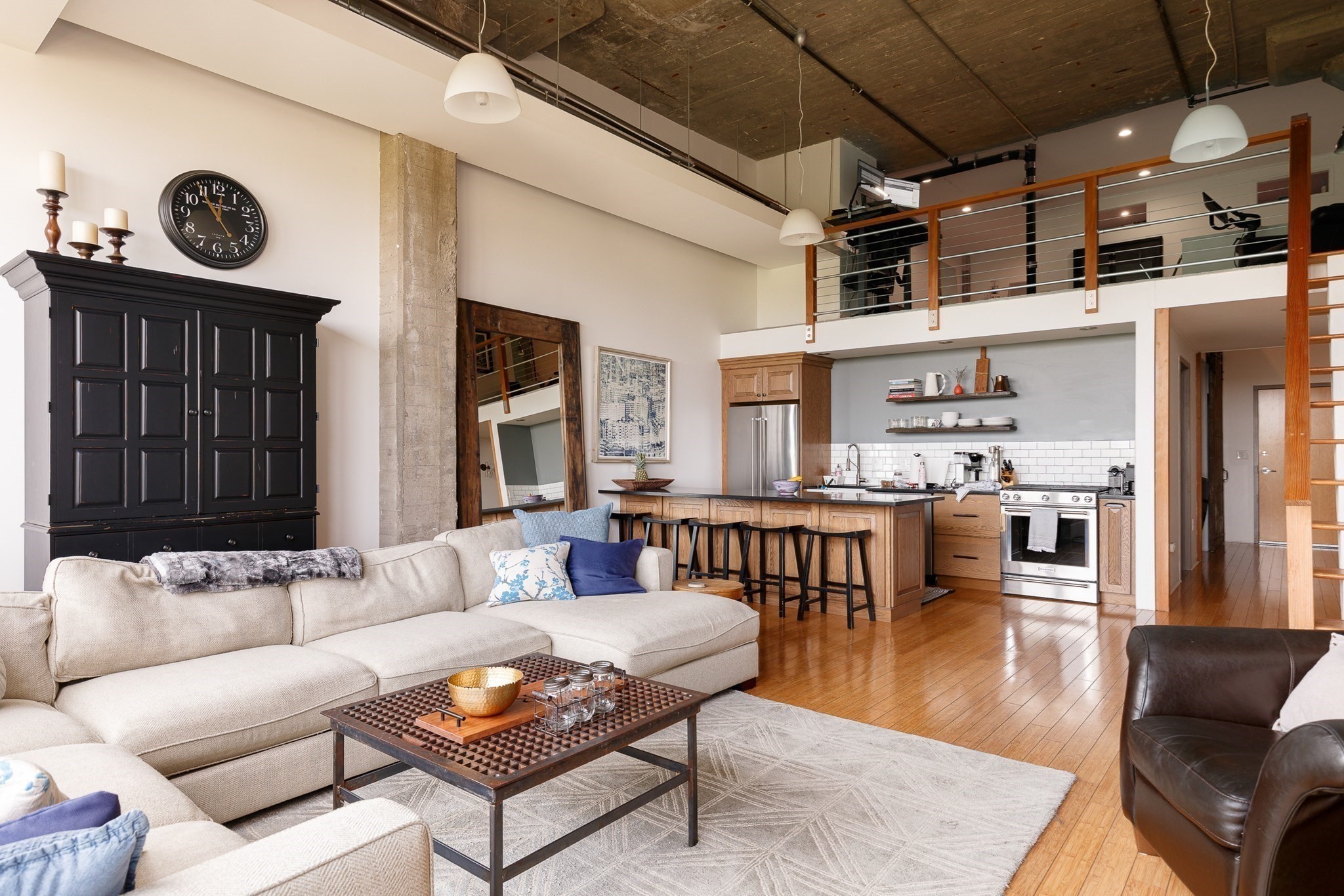 Loft living room with a cream sectional, open kitchen, exposed ceiling, and mezzanine.