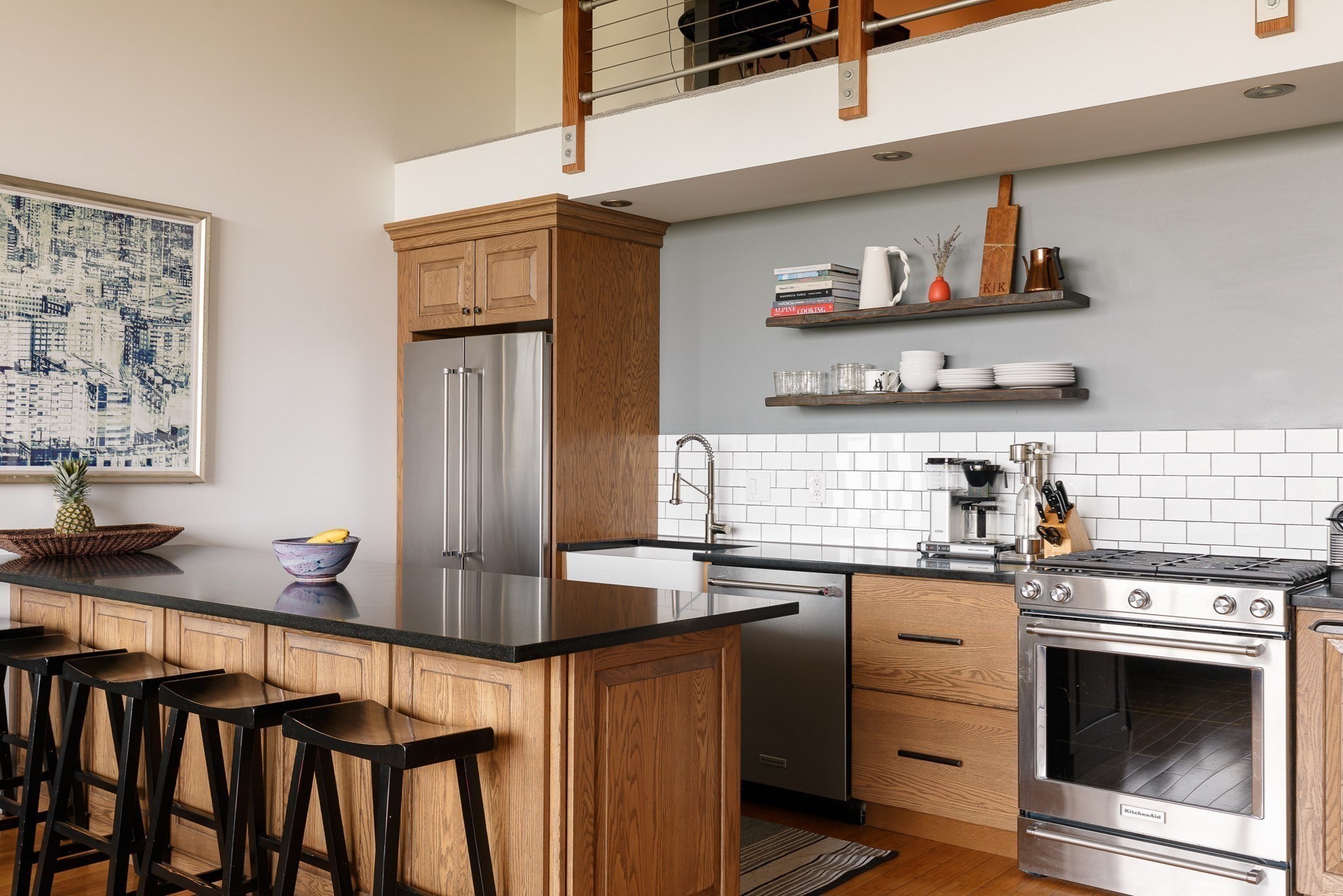 Kitchen with a wood-paneled island and bar stools, stainless steel appliances, and open shelving.