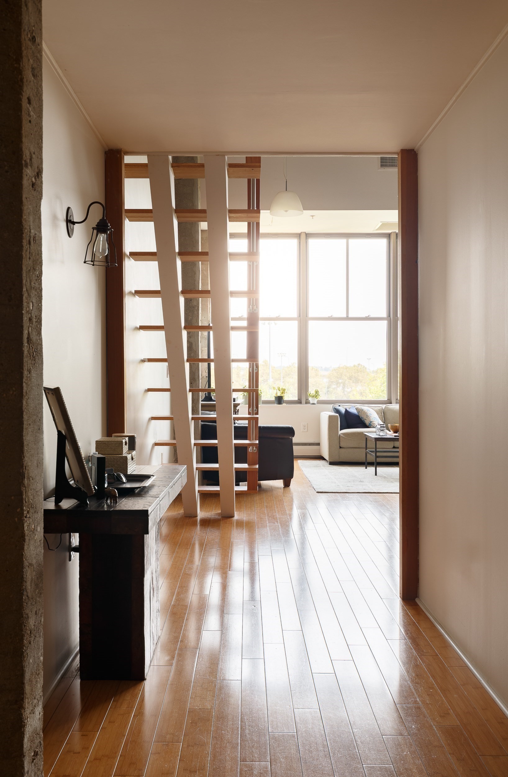 Living room with a wooden loft ladder, polished floors, and large windows.