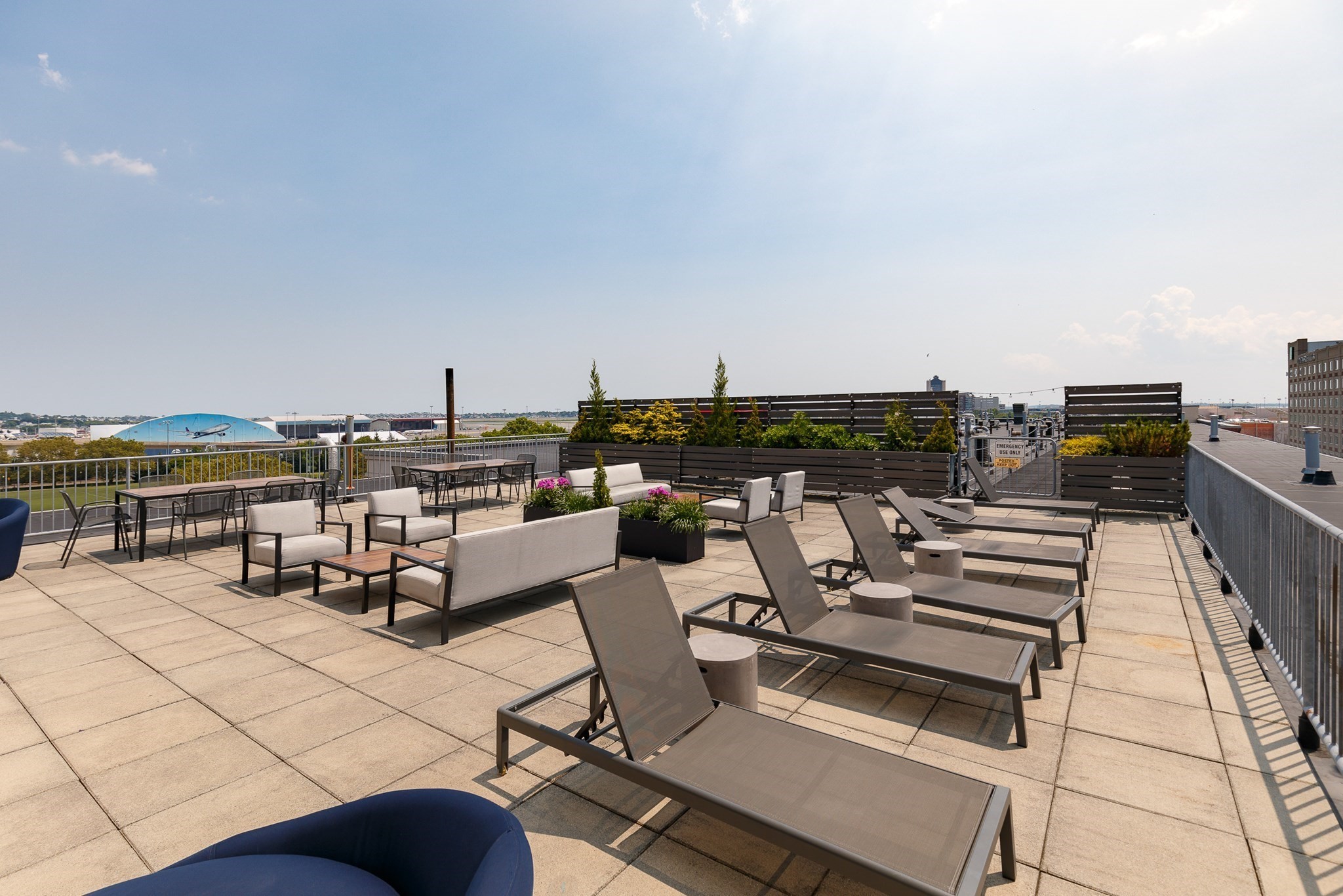 Furnished rooftop terrace with lounge seating, dining tables, and planters overlooking distant buildings.