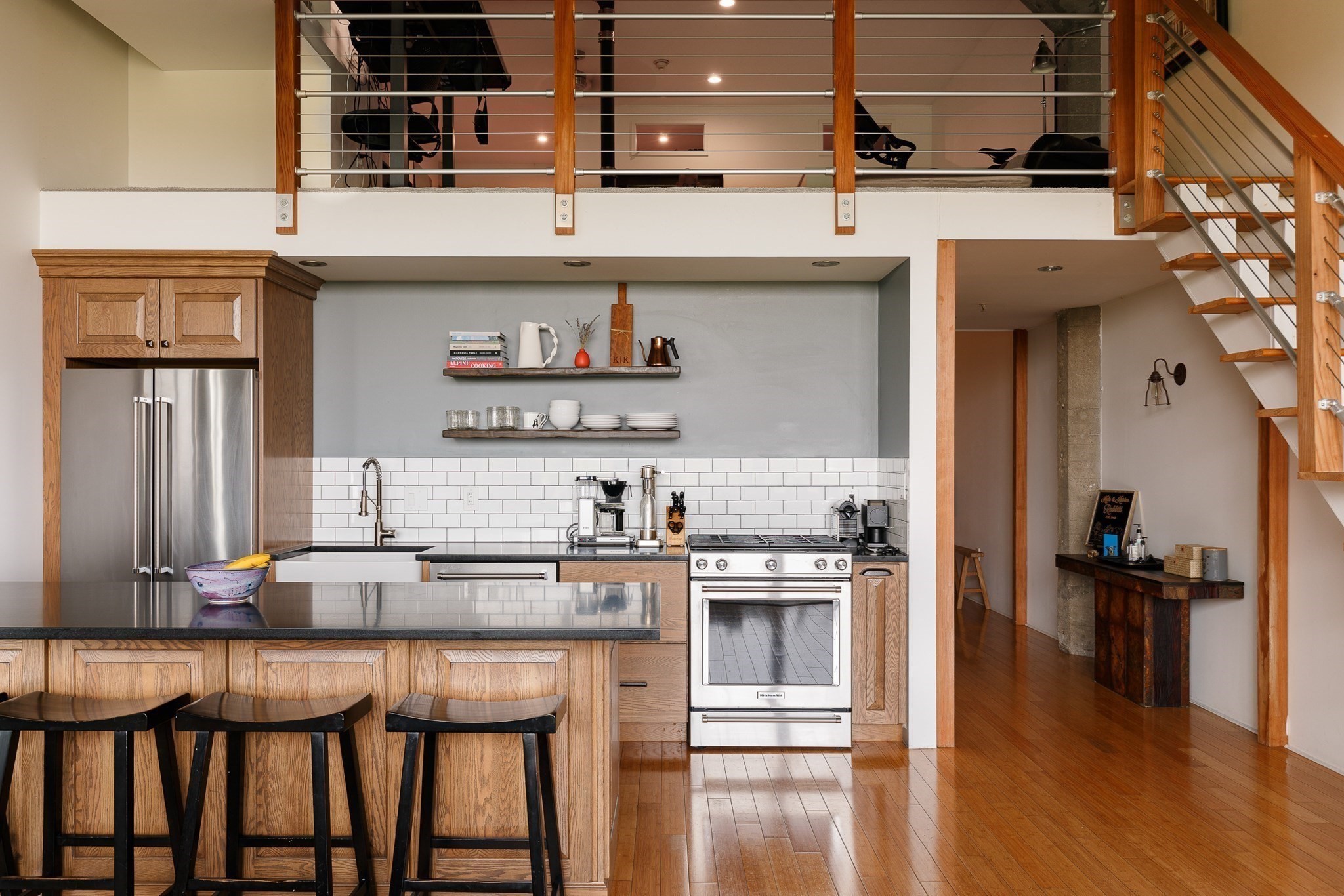 Loft kitchen with a wood island, stainless steel appliances, and a mezzanine railing above.