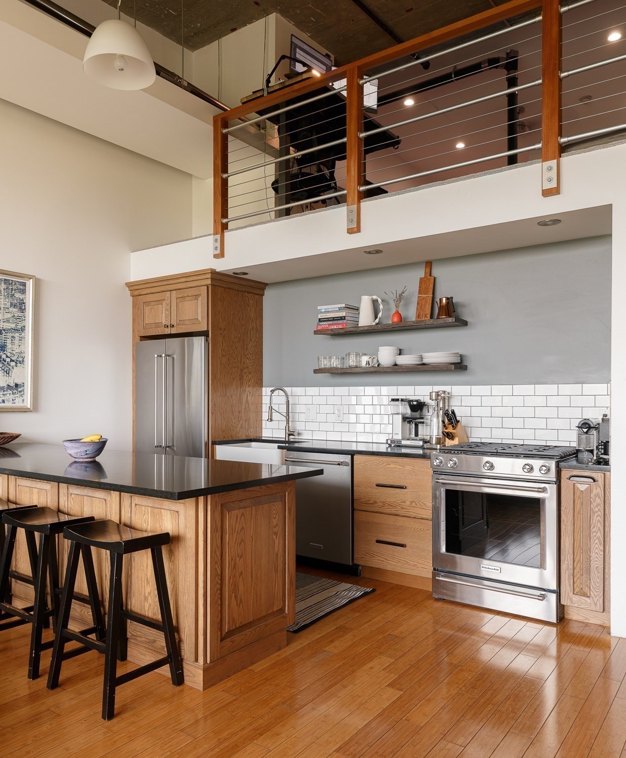 Loft kitchen with oak cabinets, a black island, stainless steel appliances, and an open mezzanine.