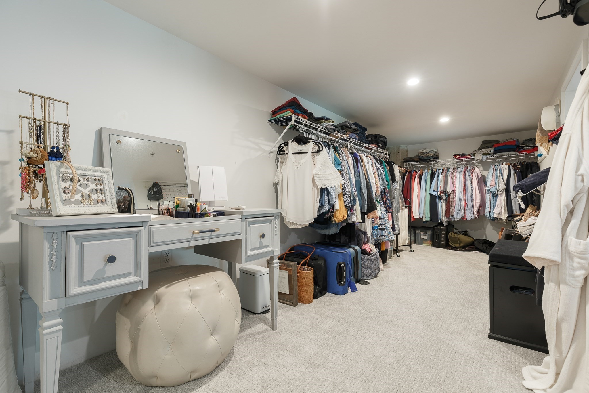 Walk-in closet with clothing racks, a pale blue vanity, and a cream tufted ottoman.
