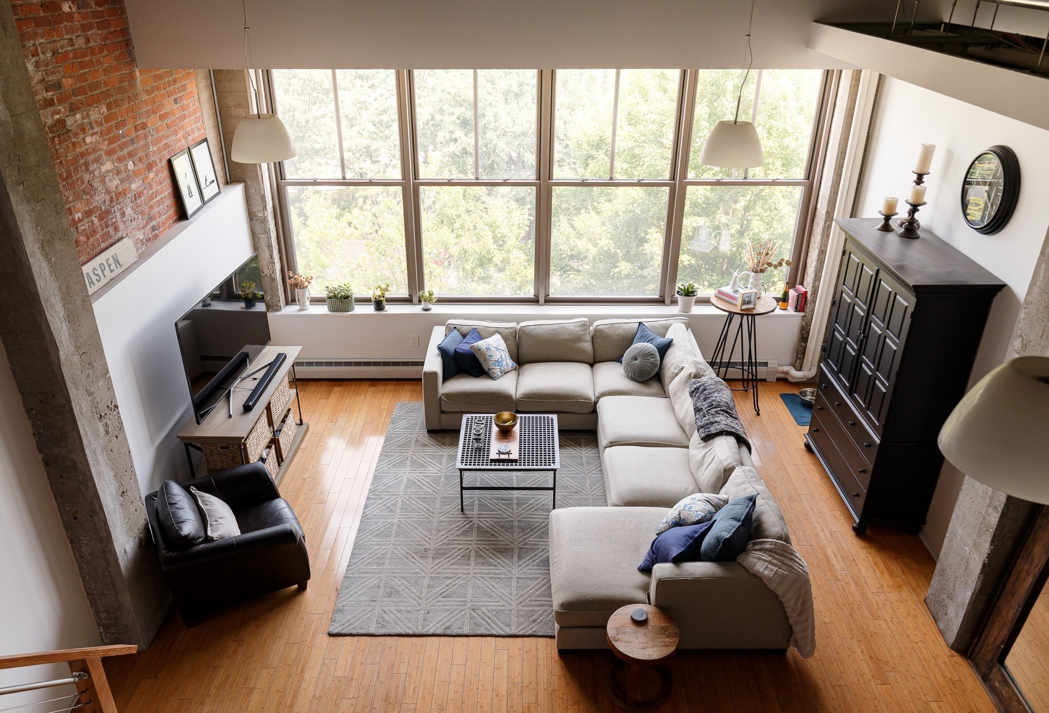 Loft living room with tall windows, exposed brick, and a large sectional sofa.