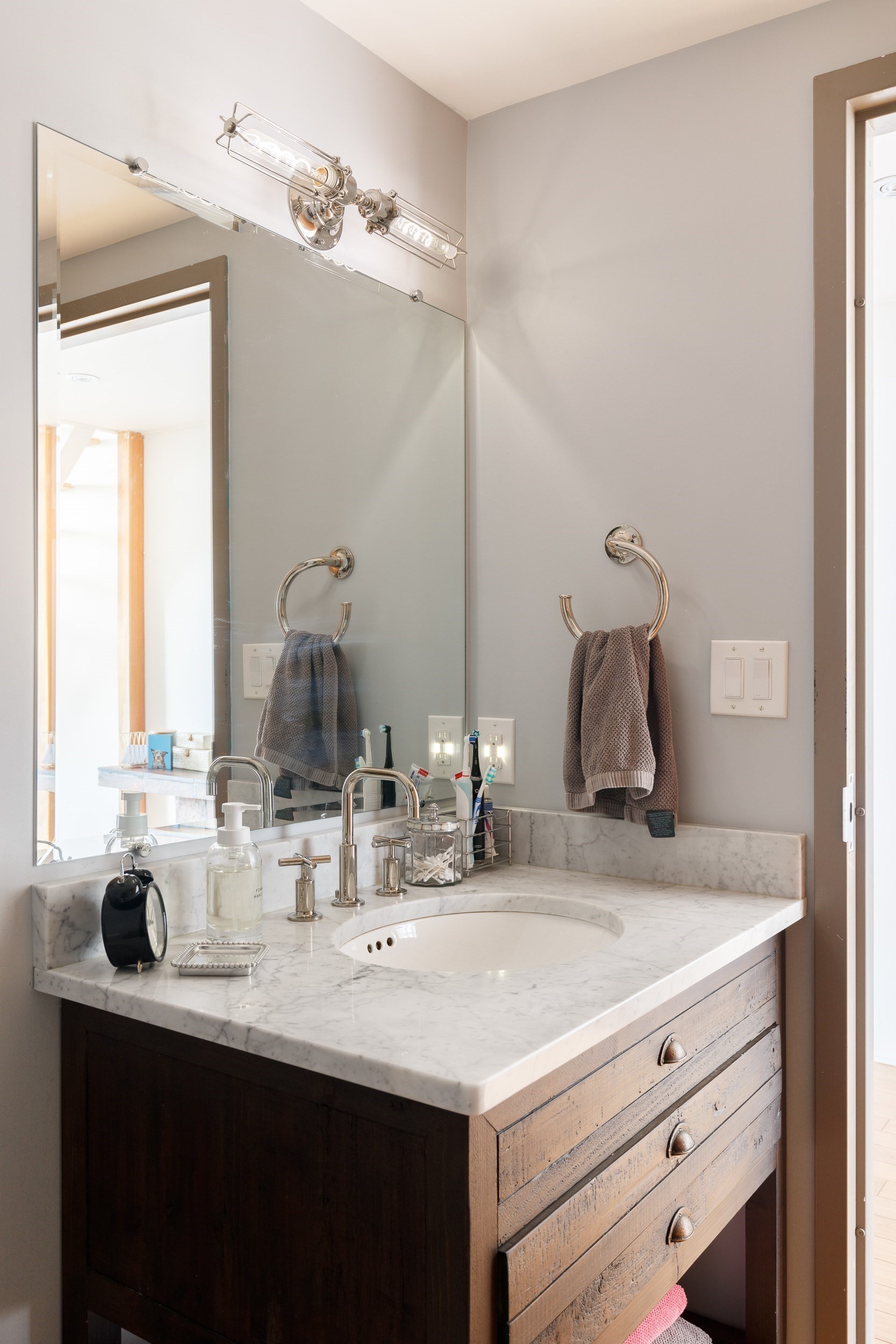 Bathroom vanity with a veined marble counter, oval sink, and rustic wood drawers.