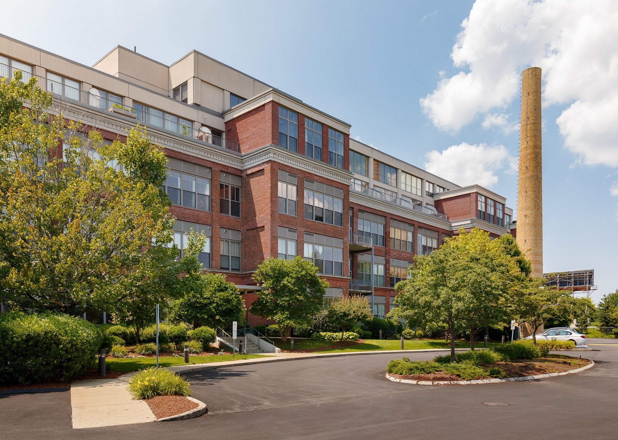 Brick apartment building with landscaped grounds and a tall brick chimney beside it.