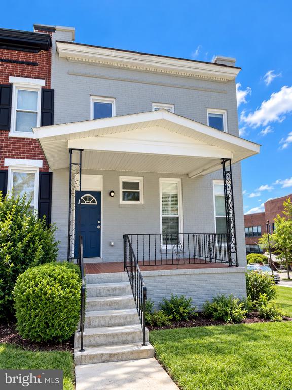 Gray rowhouse with a covered porch, blue front door, black railings, and landscaped shrubs.