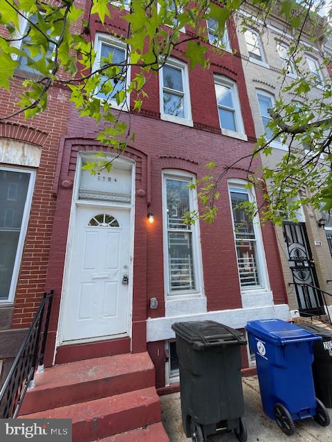 Red-brick row house at 1724 with a white door, tall windows, and leafy branches.