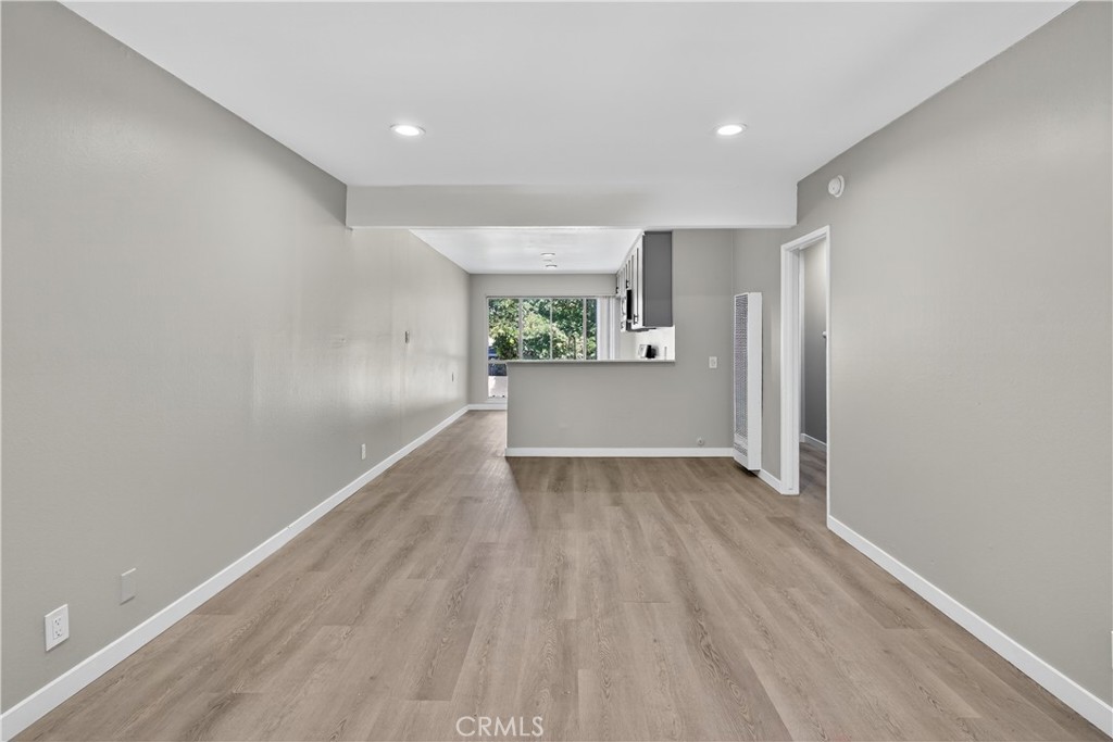 Vacant living and dining area with wood-look flooring, recessed lights, and a kitchen breakfast bar.
