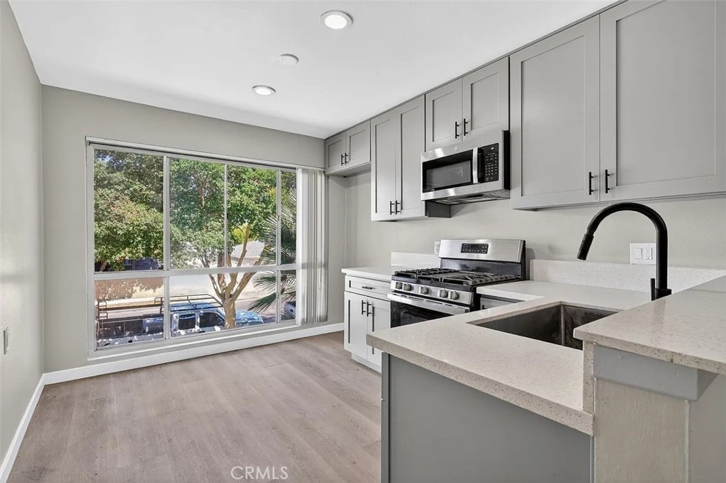 Vacant kitchen with white cabinets, quartz counters, and a large window overlooking trees.