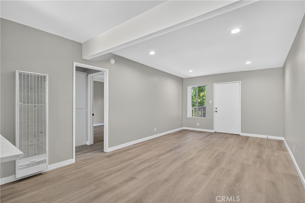 Vacant room with light wood-look flooring, recessed lights, and a wall heater.
