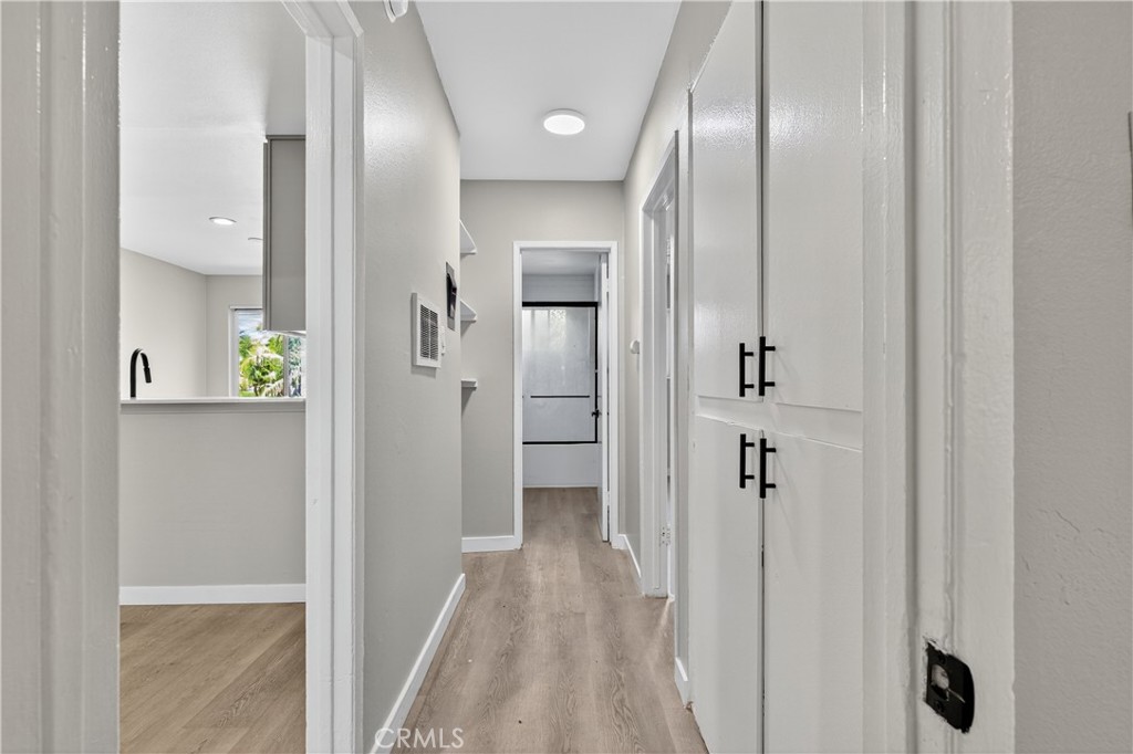 Hallway with light wood-look flooring, white built-in cabinets, and a view into the kitchen.