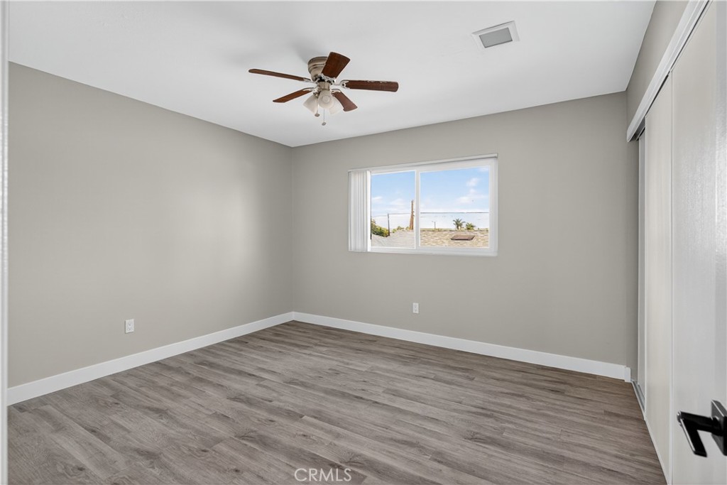 Vacant bedroom with gray wood-look flooring, a ceiling fan, and sliding closet doors.