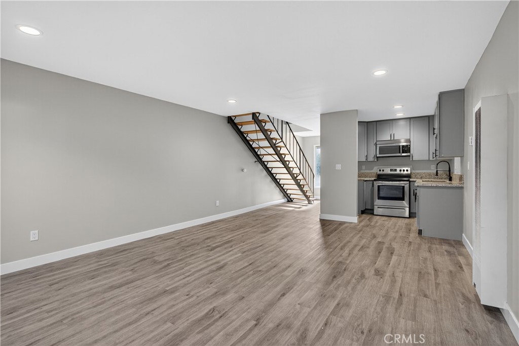 Vacant open-plan living area with gray kitchen, wood-look flooring, and an open-riser staircase.