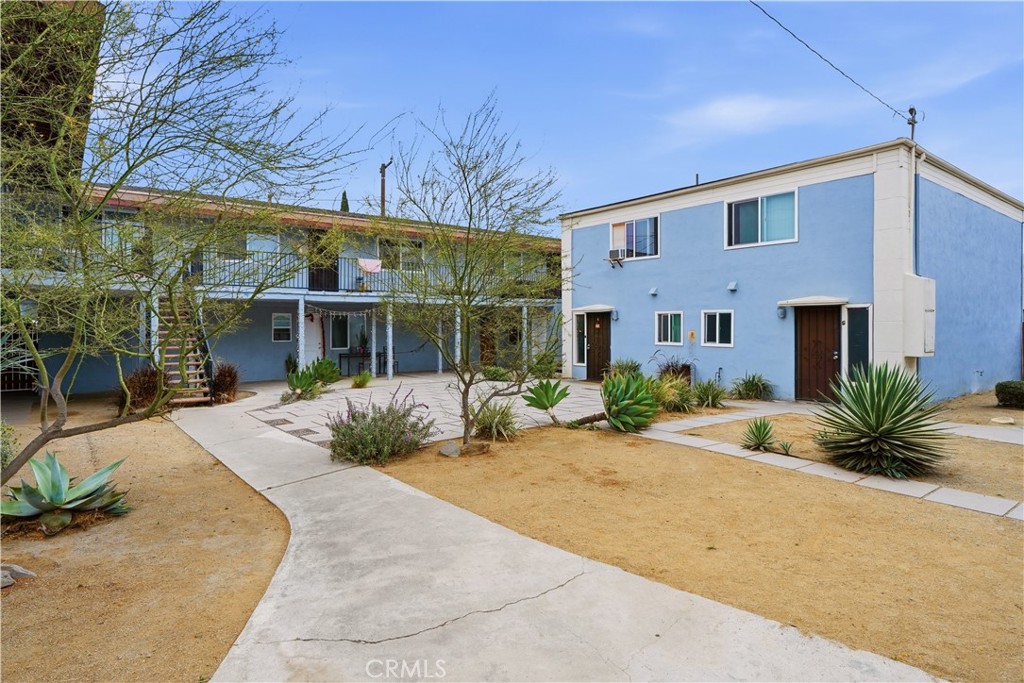 Blue two-story apartment buildings surround a courtyard with concrete walkways and drought-tolerant landscaping.