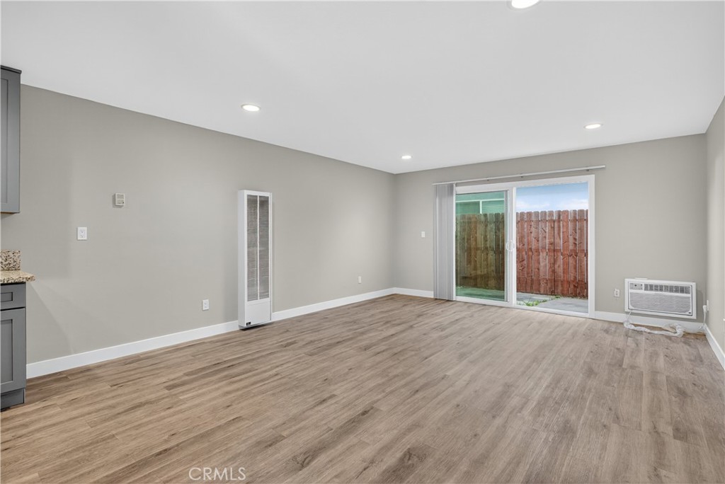 Vacant living area with wood-look floors, sliding glass doors, and a wall-mounted air conditioner.