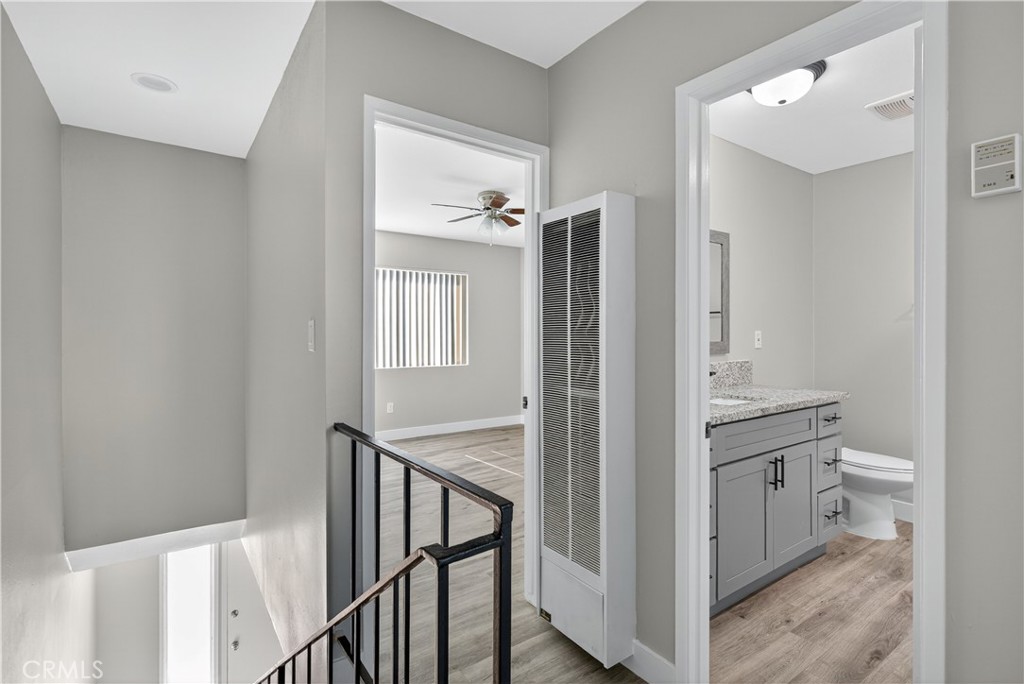 Stair landing with black railing, wood-look floors, and open views into a bedroom and bathroom.