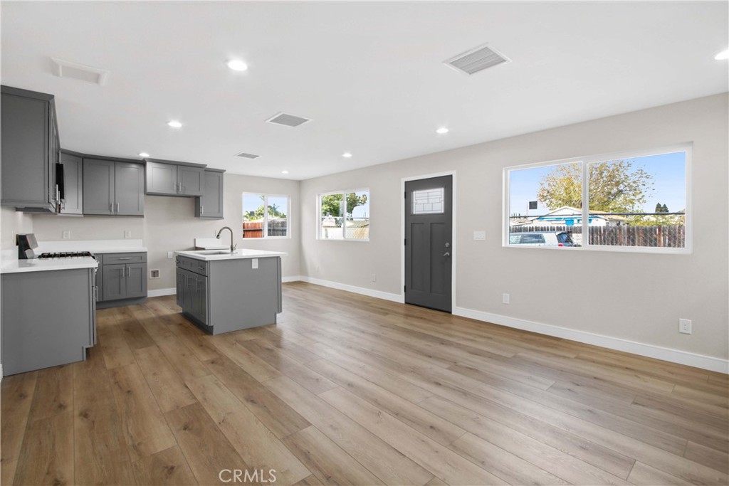Open-plan kitchen and living area with gray cabinets, a center island, and wood-look flooring.