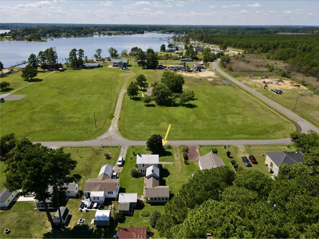 Aerial view of a grassy property beside a road, with a lake and wooded shoreline beyond.