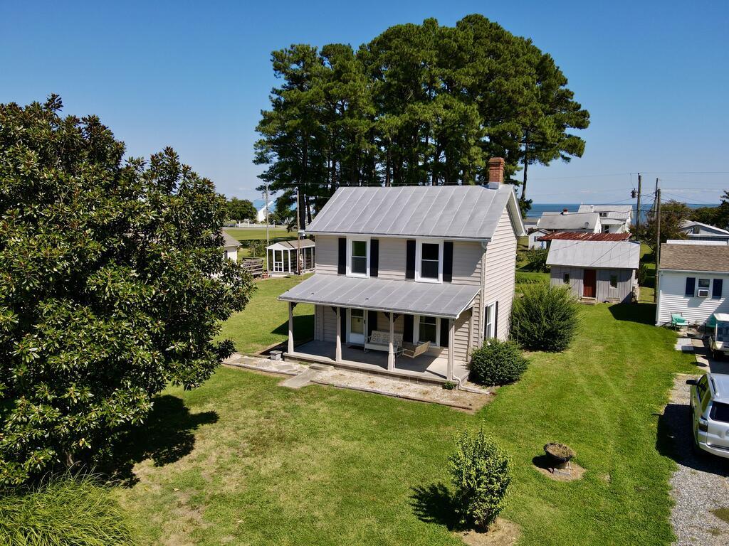 Aerial view of a two-story house with a metal roof, covered porch, and broad green lawn.