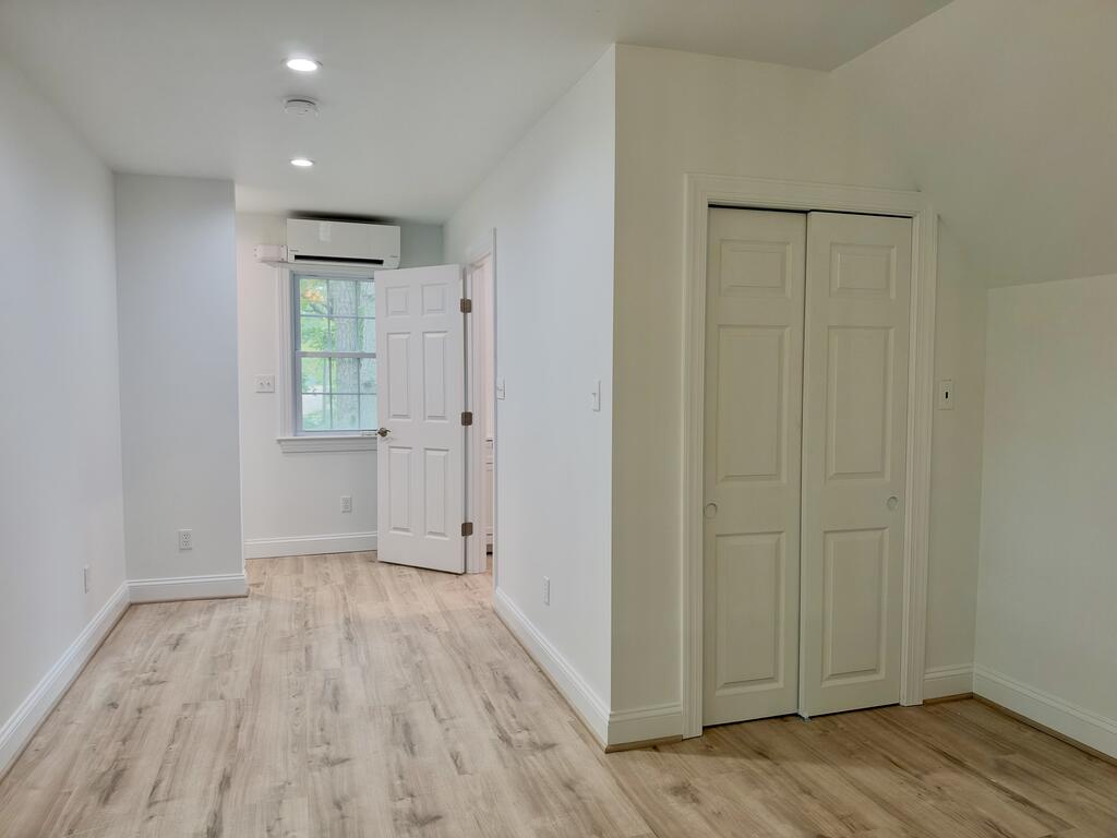 Empty room with light wood-look flooring, a window, mini-split air conditioner, and double-door closet.
