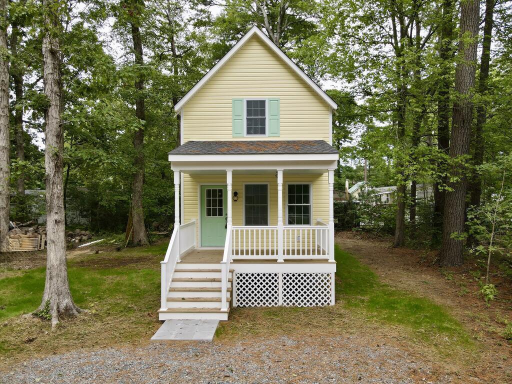 Pale yellow two-story house with mint-green accents and a white-railed porch among mature trees.