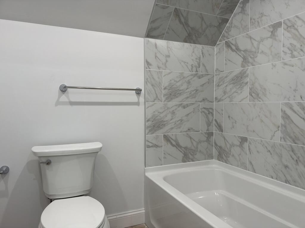 Bathroom with a white bathtub and toilet beside large gray-veined tiles.