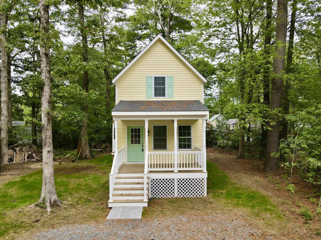 Pale yellow two-story house with a mint-green door, covered porch, and mature trees.