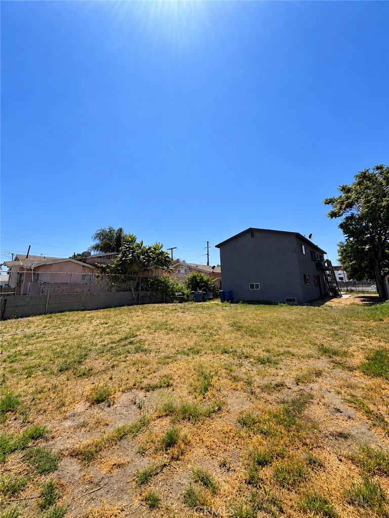 Two-story gray house beyond a dry, patchy backyard, with an exterior staircase along its side.